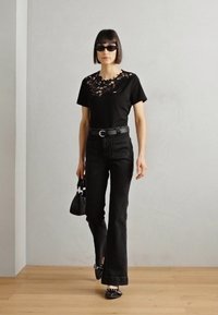 Sort t-shirt med blonde detalje ved udskæringen, parret med sorte buksede jeans med vidde. Tilbehør inkluderer en lille håndtaske og solbriller.