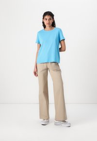 Maglietta di cotone azzurro chiaro a maniche corte, con scollatura rotonda, abbinata a pantaloni beige a gamba larga e sneakers bianche. Design semplice, vestibilità casual.