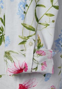 Witte linnen shirtmouw met een bloemenprint in blauw, roze en groene bloemen. Inclusief een witte knop op de manchet.