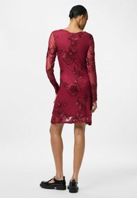 Bordó šaty s dlouhými průsvitnými rukávy, zdobené vyšívanými květinovými vzory. Délka končí nad koleny, doplněné černými botami.