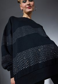 Maglione oversized nero realizzato in tessuto morbido, con un motivo a pois di paillettes argentate sul petto e sulle maniche.