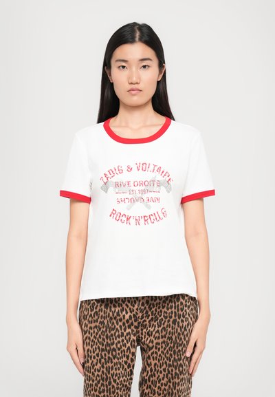 Weißes Kurzarm-T-Shirt mit rotem Saum, das glitzernden Text trägt: "Zadig & Voltaire Rock'n'Roll." Kombiniert mit braunen Leopardenmuster-Hosen.