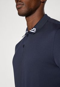 Granatowa koszulka polo z teksturowanej tkaniny, z trzema guzikami przy kołnierzyku oraz paskowym kołnierzykiem z akcentem logo.