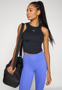 Musta hihaton urheilupaita pyöreällä pääntiellä ja valkoisella Nike-logolla, yhdistettynä korkeavyötäröisiin vaaleansinisiin legginsseihin ja mustaan kuntosalilaukkuun.