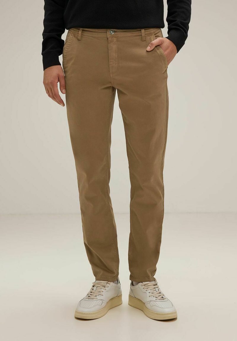 Beige chinos valmistettu puuvillasta, jossa on sileä rakenne, sivutaskut ja etupainonappi. Yhdistettynä valkoisiin lenkkareihin.