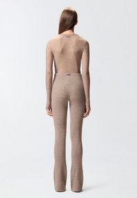 Uski prilagodljiva, dugih rukava bodi i rebraste hlace s izrezanom nogavicom u mekoj smeškastoj nijansi. Materijal ima suptilan sjaj, s logotipom na vratu i struku.