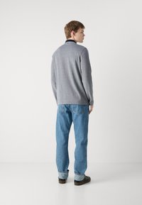 Pullover cinza de mangas longas com colarinho, apresentando detalhes escuros. Usado com jeans azuis e sapatos escuros, visto de costas.