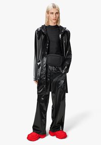 Impermeable negro brillante, pantalones a juego y una riñonera negra. Zapatos rojos gruesos con superficie texturizada y diseño audaz. Estética minimalista.