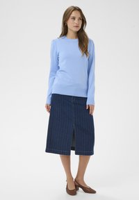 Pull bleu clair à manches longues avec poignets côtelés, associé à une jupe midi en denim foncé avec rayures verticales et une fente à l'avant.