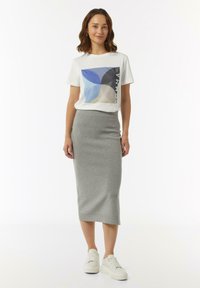 Biała koszulka z niebieskim i szarym geometrycznym nadrukiem, zestawiona z dopasowaną szaro midi spódnicą i białymi sneakersami na platformie. Gładka faktura materiału.