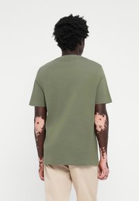 T-shirt en coton vert olive avec un col rond classique et des manches courtes, offrant une coupe décontractée et une texture lisse.