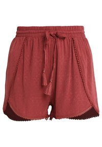 Červené kraťasy s vzorem, elastickým pasem na šňůrku, texturovanou tkaninou, ozdobnými třásněmi a vlnitými okraji. Mají boční rozparky a podšívkové detaily.