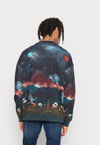 Zwarthemd met lange mouwen met een afdruk van een sterrenstelsel landschap met bergen, planeten en bloemen. Donkere kleuren met levendige ontwerpaccenten.