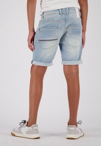 Shorts de mezclilla azul claro con dobladillos enrollados, que cuentan con dos bolsillos traseros con detalles de costura sutil, combinados con zapatillas gris y blancas.
