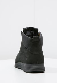 Botines de ante negro con un cuello de tela texturizada negra. Presentan una suela pronunciada, detalles en dorado y un logo grabado en el costado.