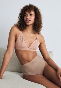 Light pink bralette with thin straps and a v-neck design paired with high-waisted, seamless underwear in a matching color. Smooth texture.
