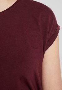 Burgundy kortärmad skjorta med rund halsringning, ribbad textur och uppvikt ärmslutar. Tyget ser mjukt och figurnära ut.