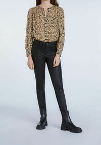 Beige und schwarzes Tigerprint-Bluse mit langen Ärmeln und Knopfleiste, kombiniert mit eleganten schwarzen Kunstlederhosen und Ankle Boots.