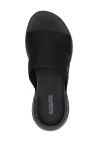 Zwarte instapsandaal met een geweven bovenkant, een textuurzool en een gevoerde voetbed, met de tekst "SKECHERS GOGA MAT" op de binnenzool.