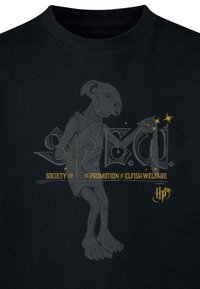 Melna kokvilnas t-kreklus ar pelēku ilustrāciju, kas attēlo elfa līdzīga tēla figūru, un zelta tekstu, kas lasa "S.P.E.W. Elfu labklājības veicināšanas sabiedrība."