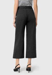 Black wide-leg trousers with an elastic waistband. Featured back pockets and smooth fabric texture. Paired with black high-heeled shoes.