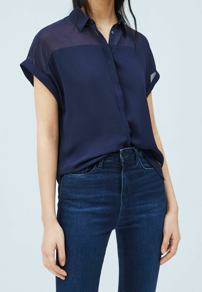 Navy blue short-sleeve shirt with a transparent upper material, button-down style, paired with dark blue skinny jeans. Smooth texture.