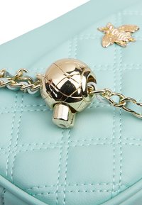 Borsa in pelle trapuntata azzurro chiaro con un elemento hardware a forma di globo dorato e una tracolla a catena, che mette in mostra una texture liscia e una cucitura dettagliata.