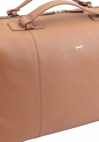 Sac à main en cuir marron avec une surface texturée, fermeture éclair et double poignées ; arbore un petit logo métallique sur le devant.