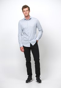 Camisa de botones azul claro con mangas largas, combinada con pantalones negros y zapatillas negras, cuenta con un cuello clásico y un corte ajustado.