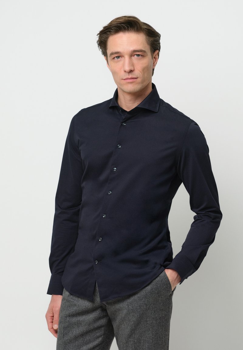 Marineblaues Langarmhemd, Knopfleiste, glatte Textur, Kentkragen, kombiniert mit grauen strukturierten Hosen.