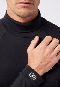 Black long-sleeve turtleneck shirt made of smooth fabric. Features a fitted design, flat seams, and a white logo on the cuff.