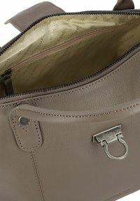Borsa in pelle taupe con chiusura in argento, manico arrotondato e fodera interna in tessuto beige con tasca con zip e stampa del marchio.