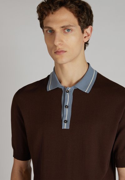 Polo de manga corta marrón con cuello azul claro que presenta dos franjas blancas, y una tapeta con tres botones negros.