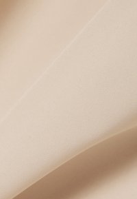 Gros plan sur un tissu beige pâle à la texture fine, délicatement plié pour créer des courbes et des ombres douces.