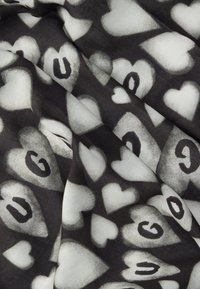 Czarno-biała tkanina z wzorem nakładających się serc i liter, tworząca dynamiczną fakturę i wizualne zainteresowanie.
