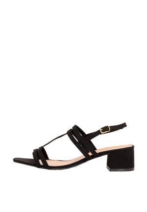 Sandal en daim noir avec un design à lanières, featuring un petit talon carré et une sangle de cheville ajustable maintenue par une boucle dorée.