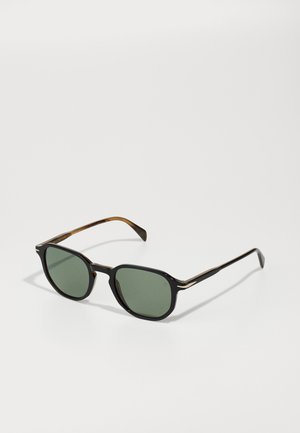 Sonnenbrille mit schwarzen und schildpattfarbenen Rahmen, grün getönten Gläsern, hexagonaler Form und schlanken Metallakzenten an den Armen.