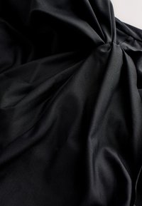 Tissu noir rassemblé et torsadé, montrant une texture lisse et des plis doux sur un fond neutre.