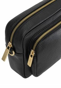 Czarna skórzana torba z dwoma złotymi zamkami, fakturowaną powierzchnią oraz prostokątnym kształtem z zaokrąglonymi krawędziami.