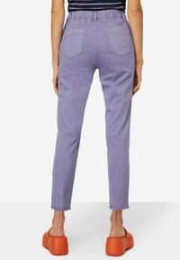 Jeans lilas con una cinturilla elástica y dos bolsillos traseros. El dobladillo presenta un borde deshilachado. Combinados con sandalias de plataforma naranjas.