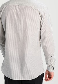 Camicia a maniche lunghe a righe in cotone grigio chiaro e bianco. Presenta un orlo curvo, polsini con bottoni e un logo discreto sul polsino.