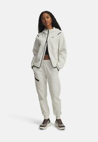 Light gray sportswear set featuring a zip-up hoodie with black accents and matching sweatpants with pockets and ribbed cuffs.