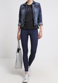 Farkkutakki hopeisilla yksityiskohdilla, musta t-paita tekstillä, tummansiniset legginsit, hopeiset lenkkarit ja teksturoitu harmaa käsilaukku.