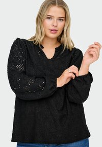 Blusa nera a occhiello con scollo a V, maniche lunghe a sbuffo e intricate fantasie floreali. Il tessuto testurizzato presenta design ritagliati.
