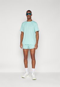 Light blue athletic t-shirt and shorts set, featuring a minimal logo, complemented by white socks and white sports shoes with green accents.