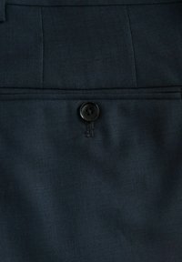 Tissu bleu foncé avec une surface texturée, présentant un bouton noir à quatre trous, placé sur des vêtements sur mesure.