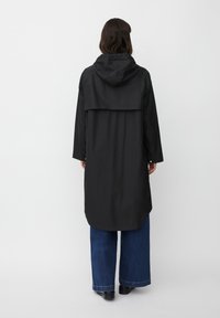 Impermeabile nero leggero con cappuccio, maniche lunghe e orlo leggermente curvato. Presenta una vestibilità ampia e una texture liscia.