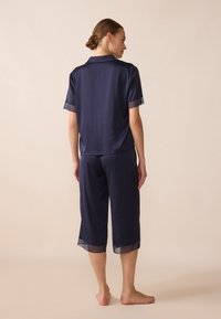 Tumši zilas pidžamu komplekts ar īsām piedurknēm un mežģīņu apdari. Iekļauj vaļīgas, īsas bikses un gludu audumu. Nav redzamu rakstu vai piederumu.