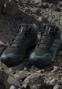 Sorte vandresko med en tekstureret overflade, der har grønne detaljer og en holdbar gummisål, designet til godt fodfæste på stenede terræner.