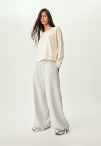 Haut crème à manches longues avec une coupe décontractée, associé à un pantalon de jogging gris à pattes larges. Tissu lisse, design décontracté et détails subtils à l'ourlet.